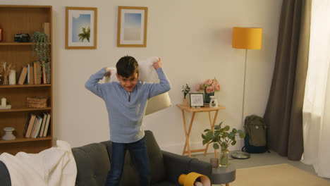 Disruptive-Young-Boy-Behaving-Badly-At-Home-Jumping-On-Sofa-And-Throwing-Cushions-Around-Lounge-3